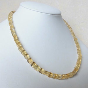 May include: A gold necklace made of faceted citrine beads. The beads are square shaped and have a translucent appearance.