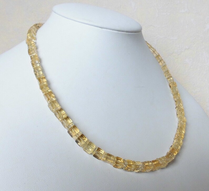 May include: A gold necklace made of faceted citrine beads. The beads are square shaped and have a translucent appearance.
