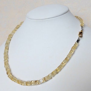 May include: A gold and clear citrine gemstone necklace with a gold clasp. The necklace is made of square-shaped beads.