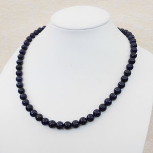 May include: A dark blue beaded necklace made of round beads. The necklace is displayed on a white mannequin bust.