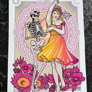 May include: A colorful poster featuring a skeleton dancing with a woman in a yellow and orange dress. The background includes a sun, moon, and floral design. Text at the bottom reads "The Gorge 2023 July 7th & 8th."