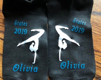 May include: Pair of black ankle socks with a white silhouette of a gymnast doing a handstand. The socks have the text "States 2019" and "Olivia" in blue.