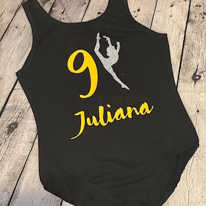 May include: Black leotard with a yellow number 9 and a silver silhouette of a dancer. The name Juliana is written in yellow below the number.