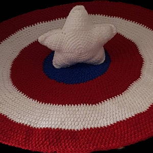 May include: A handmade crochet shield in red, white, and blue, with a white star in the center. The shield is round, with concentric rings of color. The star is five-pointed and also crocheted.