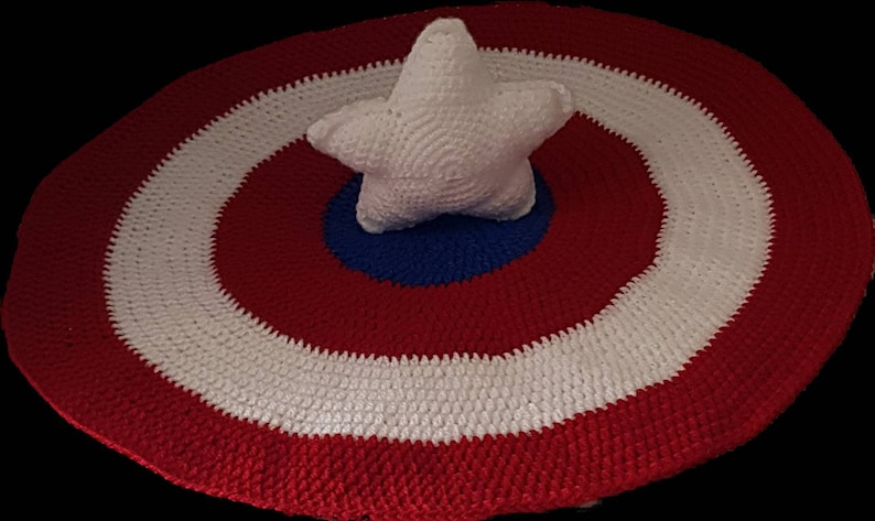 May include: A handmade crochet shield in red, white, and blue, with a white star in the center. The shield is round, with concentric rings of color. The star is five-pointed and also crocheted.