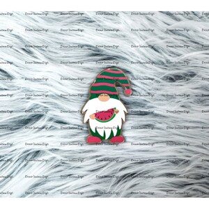 May include: A wooden gnome figurine with a red and white striped hat and a white beard. The gnome is holding a slice of watermelon in its hands. The gnome is standing on a white furry background.