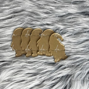 May include: Four gold-coloured gnome ornaments with white beards and red hats. The gnomes are standing on a grey fuzzy surface.
