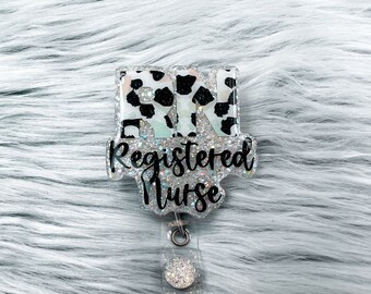 Puede incluir: Un portatarjetas brillante con el texto "Registered Nurse". La insignia tiene un diseño de estampado de vaca con las letras "RN". El portatarjetas es transparente con un respaldo de purpurina plateada.