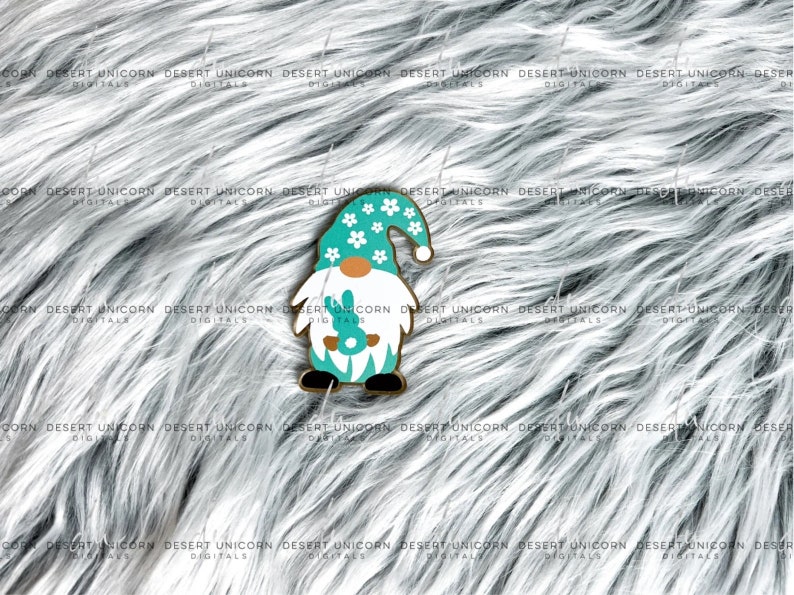 May include: A turquoise gnome with a white hat and white flowers. The gnome is holding a green bunny in its hands. The gnome is standing on a white fluffy surface.