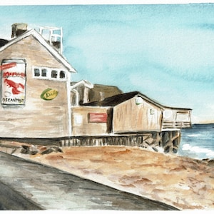 May include: A watercolor painting of a wooden building on the coast. The building has a red sign with the words "Ocean Spray" on it. The building is on stilts over the water. The water is blue and there is a sandy beach in the foreground.