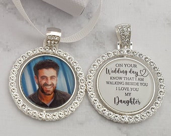 May include: A silver pendant with a clear photo insert and a rhinestone border. The pendant is attached to a white satin ribbon. The back of the pendant has a message that reads "On your Wedding day Know that I am walking beside you I love you My Daughter".