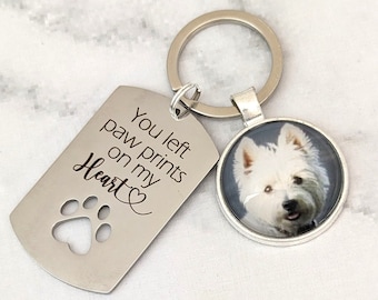 May include: A silver keychain with a dog paw print cutout and the text "You left paw prints on my heart" engraved on the tag. A round silver charm with a photo of a white dog is attached to the keychain.