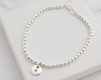 May include: A silver beaded bracelet with a small silver charm that has the letter 'A' engraved on it.