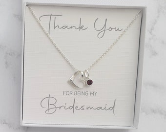 May include: A silver necklace with a heart charm and a small red gemstone. The necklace is in a white box with the text "Thank You for being my Bridesmaid".