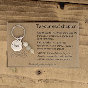 パーソナライズされた「To Your Next Chapter」キーホルダー。新しい仕事、新しい学校、卒業、新しい家、結婚、出産など、次の章へと進みましょう。