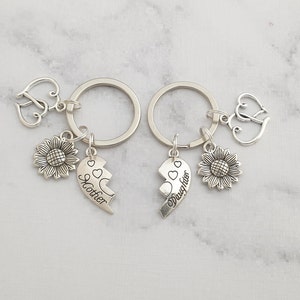 May include: Two silver keychains with a sunflower charm, a heart charm, and a split heart charm that says "Mother" and "Daughter".