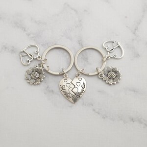 May include: Two silver keychains with sunflower charms and a split heart charm that reads "Mother" and "Daughter".