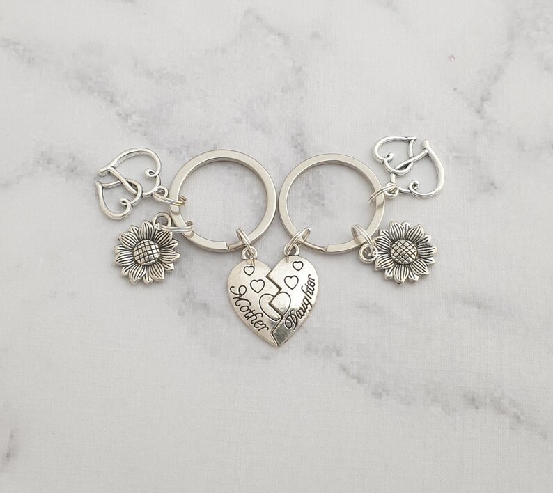 May include: Two silver keychains with sunflower charms and a split heart charm that reads "Mother" and "Daughter".