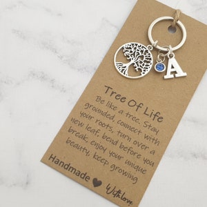 May include: A silver tree of life keyring with a blue crystal charm and a silver letter A charm. The keyring is attached to a brown card with the text "Tree Of Life" and a quote about being like a tree. The card also says "Handmade with love."