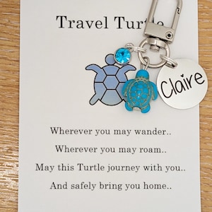 May include: A silver keyring with a blue turtle charm and a round tag with "Claire" on it. The card says "Travel Turtle" and a poem about safe travels.