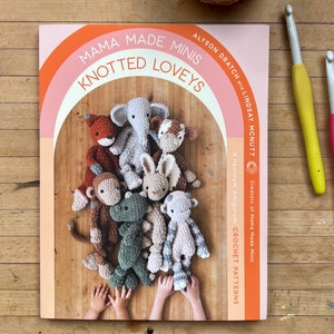 May include: A book titled "Mama Made Minis Knotted Loveys" with a colorful rainbow arch design. The cover features 16 crochet amigurumi patterns for creating adorable animal toys.
