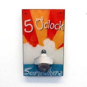 May include: A rectangular wall-mounted bottle opener with a sunset design. The artwork features the text "5 O'clock Somewhere" in white against a red, orange, and blue background. The bottle opener is silver.