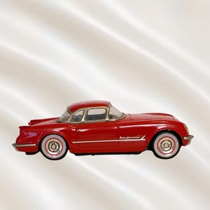 May include: A red vintage-style toy car with white-walled tires. The car has a hardtop and gold trim around the windows. The car's body is a glossy red, and the wheels have a classic design.