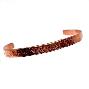 May include: A copper cuff bracelet with a textured surface. The open-ended bracelet has a hammered appearance and is designed to be worn on the wrist. The bracelet is a warm, reddish-brown color.