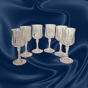 May include: Set of seven clear crystal wine glasses with a diamond-cut pattern. Each glass has a stemmed base and a rounded bowl. The glasses are arranged on a dark blue, satin-like background.