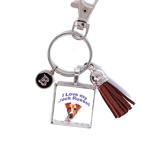 May include: A silver-toned metal keychain featuring a square pendant with a Jack Russell terrier illustration and the text I Love my Jack Russel, a small circular charm with the letter B, and a brown faux leather tassel attached to a split ring.