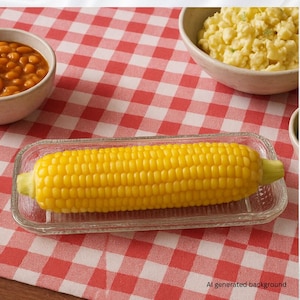May include: A cooked ear of yellow corn on a clear glass dish, with a red and white checkered tablecloth in the background. Bowls of baked beans and potato salad are also visible.