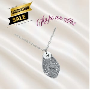 May include: Silver-toned necklace with a pendant shaped like a spoon, featuring floral detailing. A small, round charm with the letter "W" is attached. The image also includes text that says "Liquidation Sale" and "Make an offer".