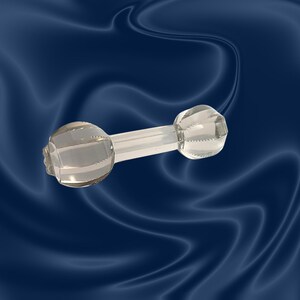 May include: A clear glass dumbbell-shaped object with a central rod connecting two faceted, spherical ends. The ends have horizontal ridges. The object is displayed against a dark blue, wavy background.