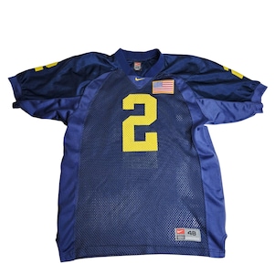 Pode incluir: Uma camisola de futebol azul marinho com o número 2 amarelo na frente. A camisola tem um patch da bandeira americana e o logótipo da Nike. Tamanho 48.