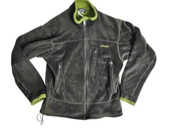 May include: A gray fleece jacket with a green collar and trim. The jacket has a full zipper, two zippered pockets, and the Patagonia logo on the chest. The jacket is made of a soft, fuzzy material.