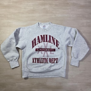 Może przedstawiać: Szara bluza Hamline University z bordowymi napisami. Tekst zawiera "HAMLINE UNIVERSITY" nad "XXL" i "ATHLETIC DEPT". Bluza z okrągłym dekoltem ma długie rękawy i luźny krój.