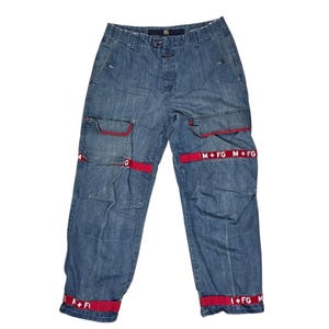 May include: Blue denim cargo trousers with red detailing. The trousers have multiple pockets and red bands with white text reading "M+FG". The red bands are on the pockets and around the ankles.
