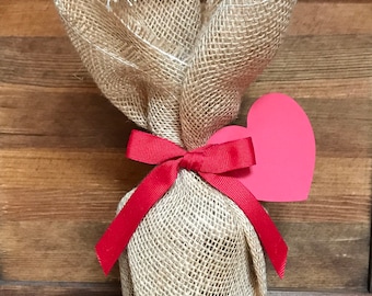 May include: A burlap gift bag tied with a red ribbon and a pink paper heart.