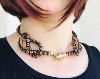 Puede incluir: Un collar de serpiente de cuentas negras y doradas con un dije de cabeza de serpiente dorada. El collar mide 27 pulgadas (68,58 cm) de largo.