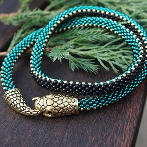 May include: A beaded snake necklace with a gold snake head clasp. The necklace is made with black and teal beads.
