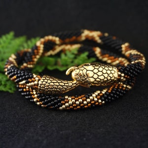 May include: A beaded snake necklace with a gold snake head charm. The necklace is black and gold and is coiled up on a black surface.