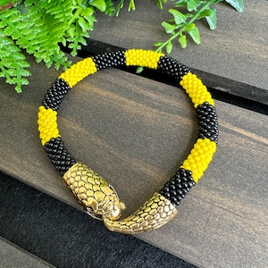 May include: A black and yellow beaded bracelet with a gold snake head clasp.