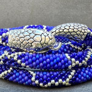 May include: A blue and silver beaded bracelet with a snake head charm. The bracelet is made of small, round beads and is wrapped around itself several times.