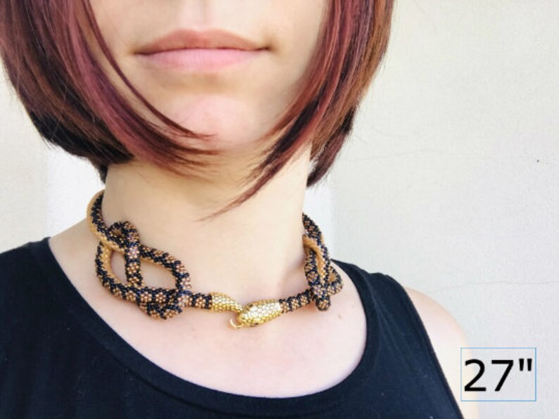 Pu&ograve; includere: Una collana di serpente con perline nere e dorate con un ciondolo a forma di testa di serpente dorata. La collana &egrave; lunga 27 pollici.