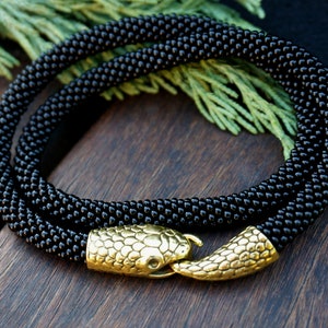 May include: A black beaded necklace with a gold snake clasp. The necklace is made of small, round beads and is about 18 inches long.