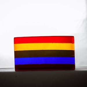 May include: A rectangular glass block with four horizontal stripes in red, yellow, brown, and blue.