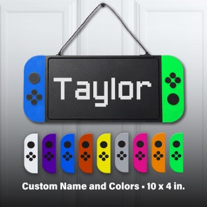 May include: A black and green Nintendo Switch door hanger with the name "Taylor" in white pixelated letters. The hanger is 10 inches by 4 inches and comes in a variety of colors.