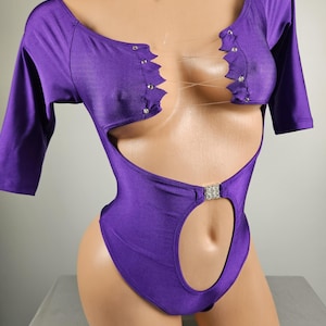 May include: Purple bodysuit with a cut-out design and rhinestone accents. The bodysuit has short sleeves and a scoop neck.