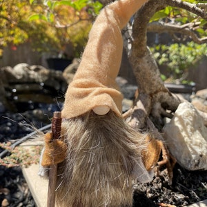 May include: A brown gnome with a long, shaggy beard and a brown felt hat. The gnome is holding a wooden walking stick and is standing on a brown surface. The text "1. Hiker Front" is visible in the image.