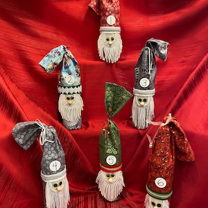 May include: Six wine bottle gift bags decorated as gnomes with different fabric patterns and numbers 1 through 6. The gnomes have white beards and white trim around their hats.